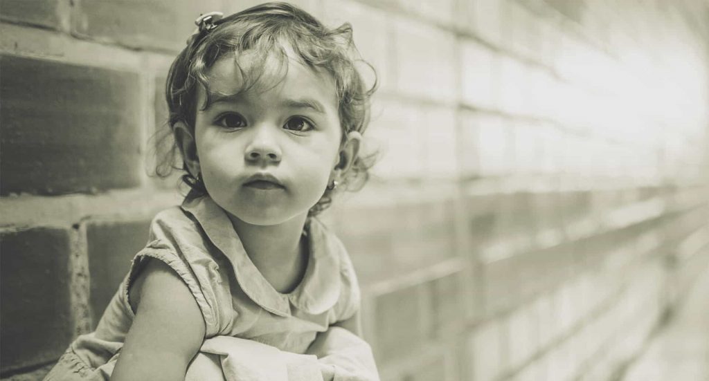 Toddler girl with curly hair by brick wall