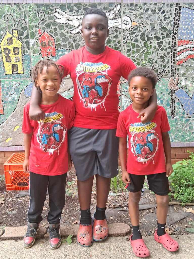 Three children in red Spider-Man shirts smiling