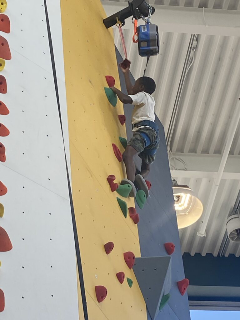 Child climbing indoor rock wall with harness